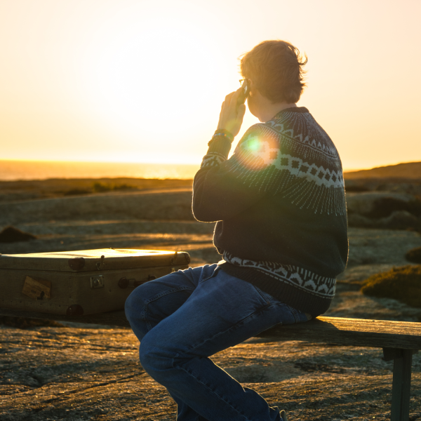Person pratar med någon i telefon med en stödlinje vid en solnedgång bredvid havet på en klippa.